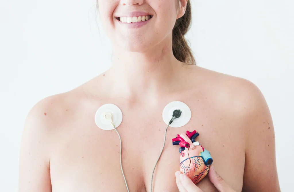 female with electrocardiogram leads hand with figurine heart